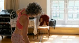 Older adult performing gentle stretching beside a chair in a bright, uncluttered home.